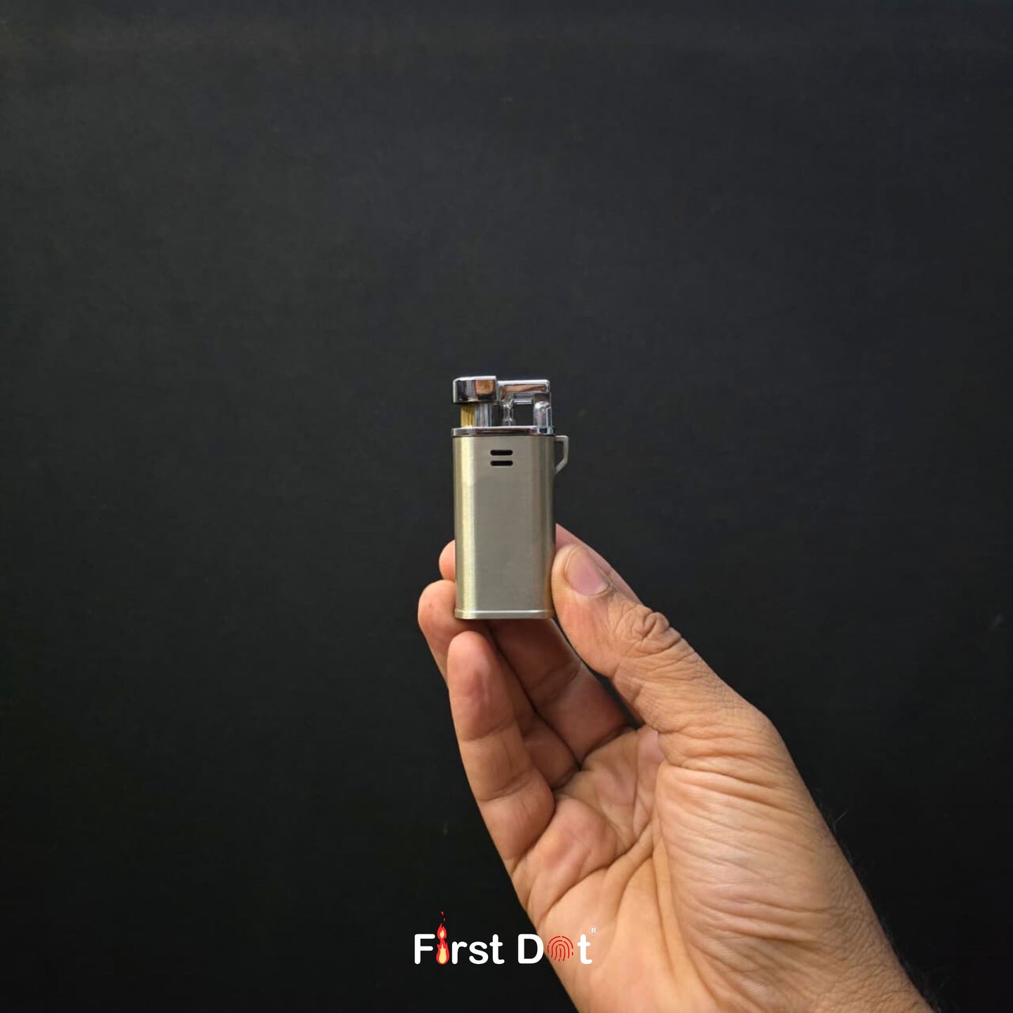 Hand holding a small metallic lighter against a black background with 'First Dot' branding.