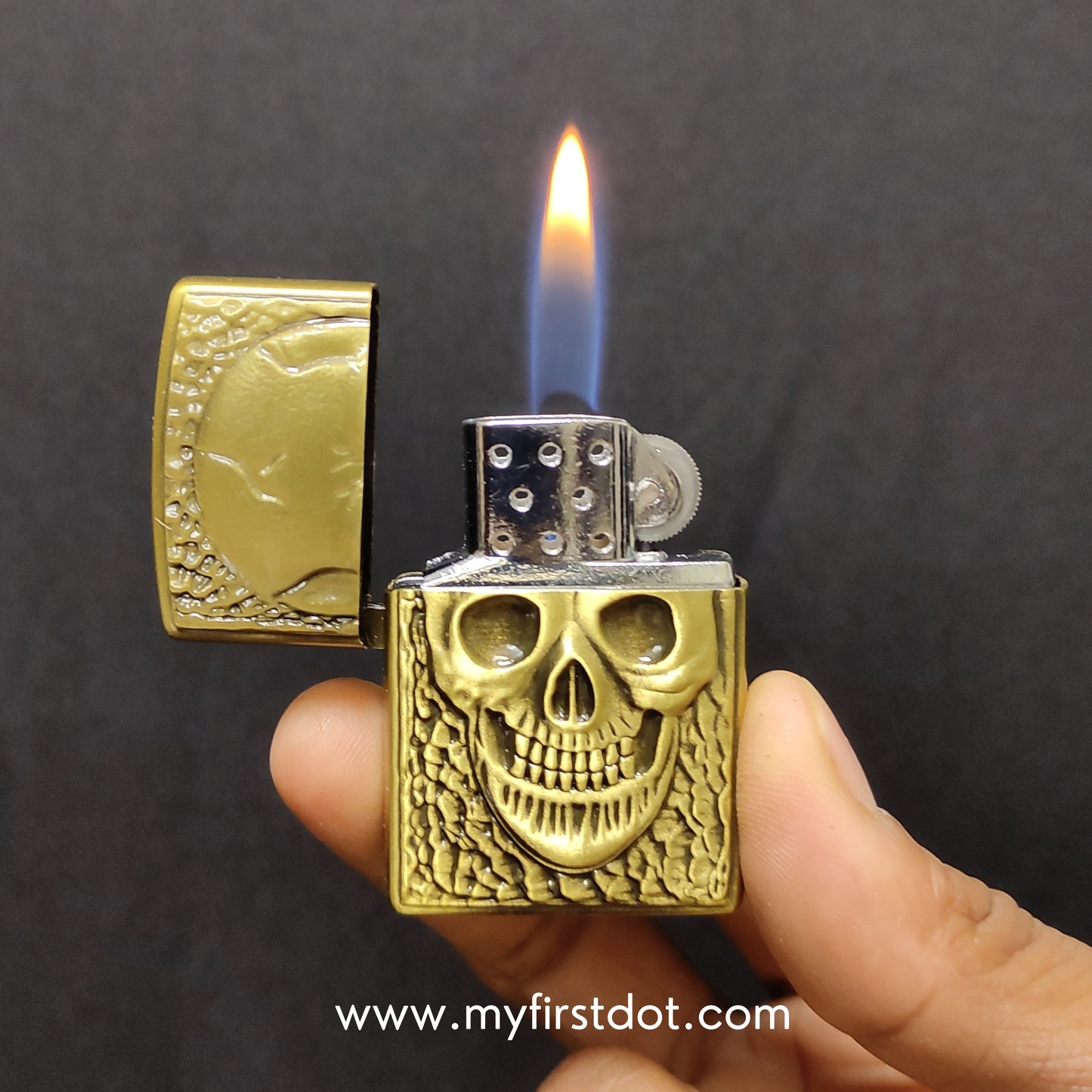 Gold skull design lighter being held with flame against a dark background