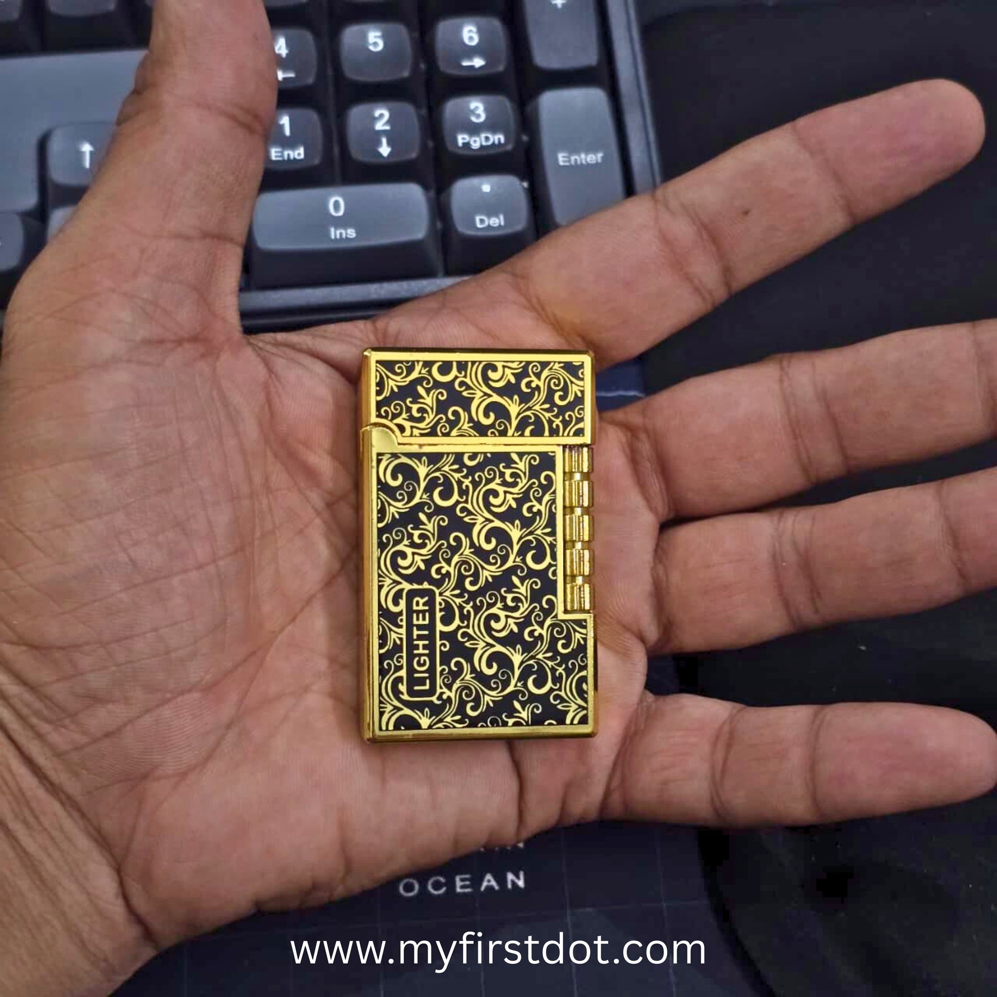 Gold lighter with intricate designs held in a hand, keyboard in the background