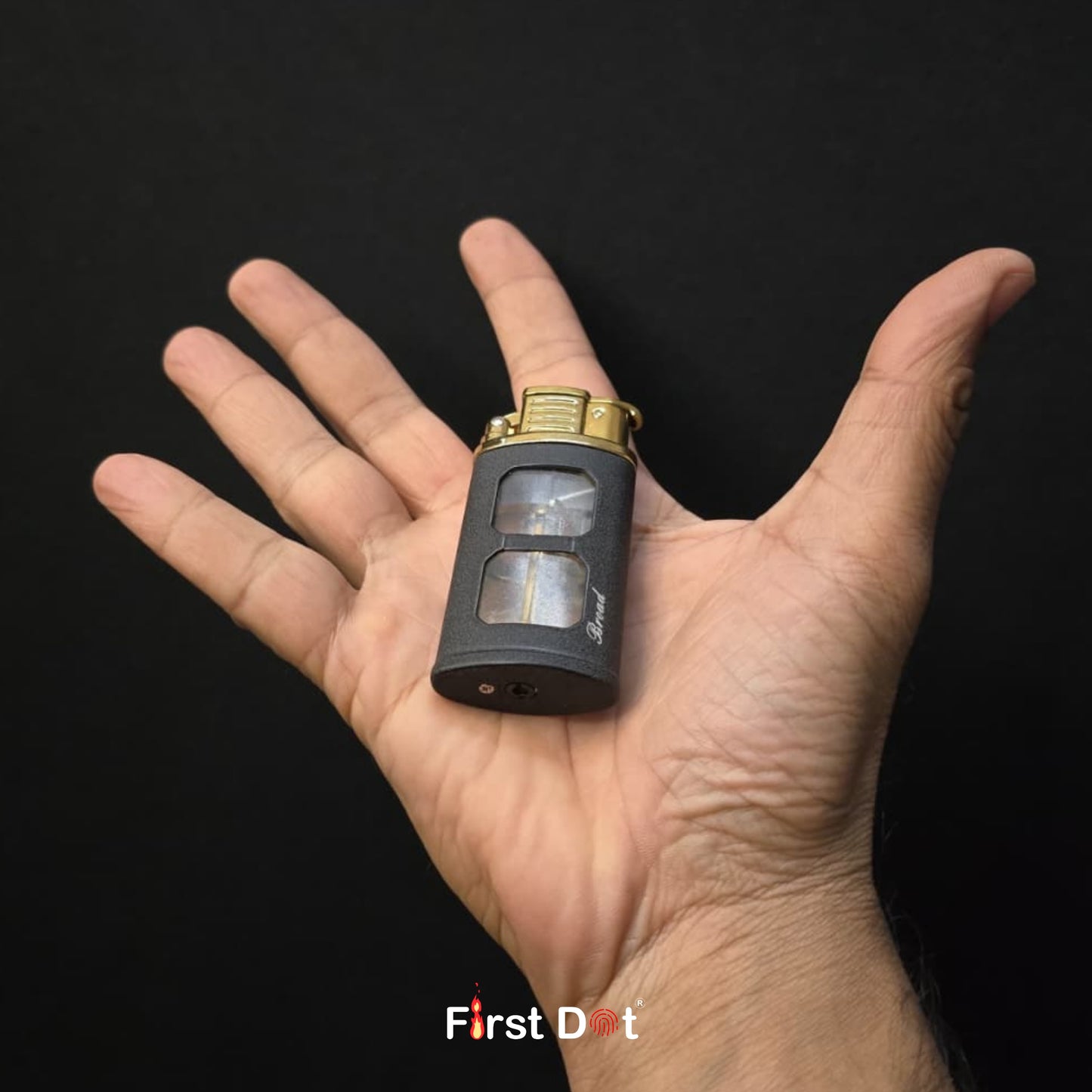 Hand holding a small black and gold device with 'First Dot' branding on a dark background