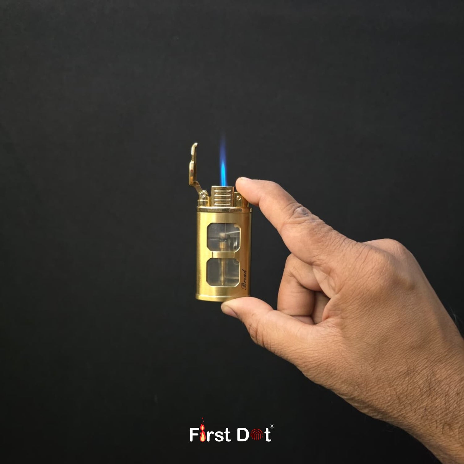 Hand holding a gold lighter with a blue flame against a black background, featuring the 'First Dot' brand.