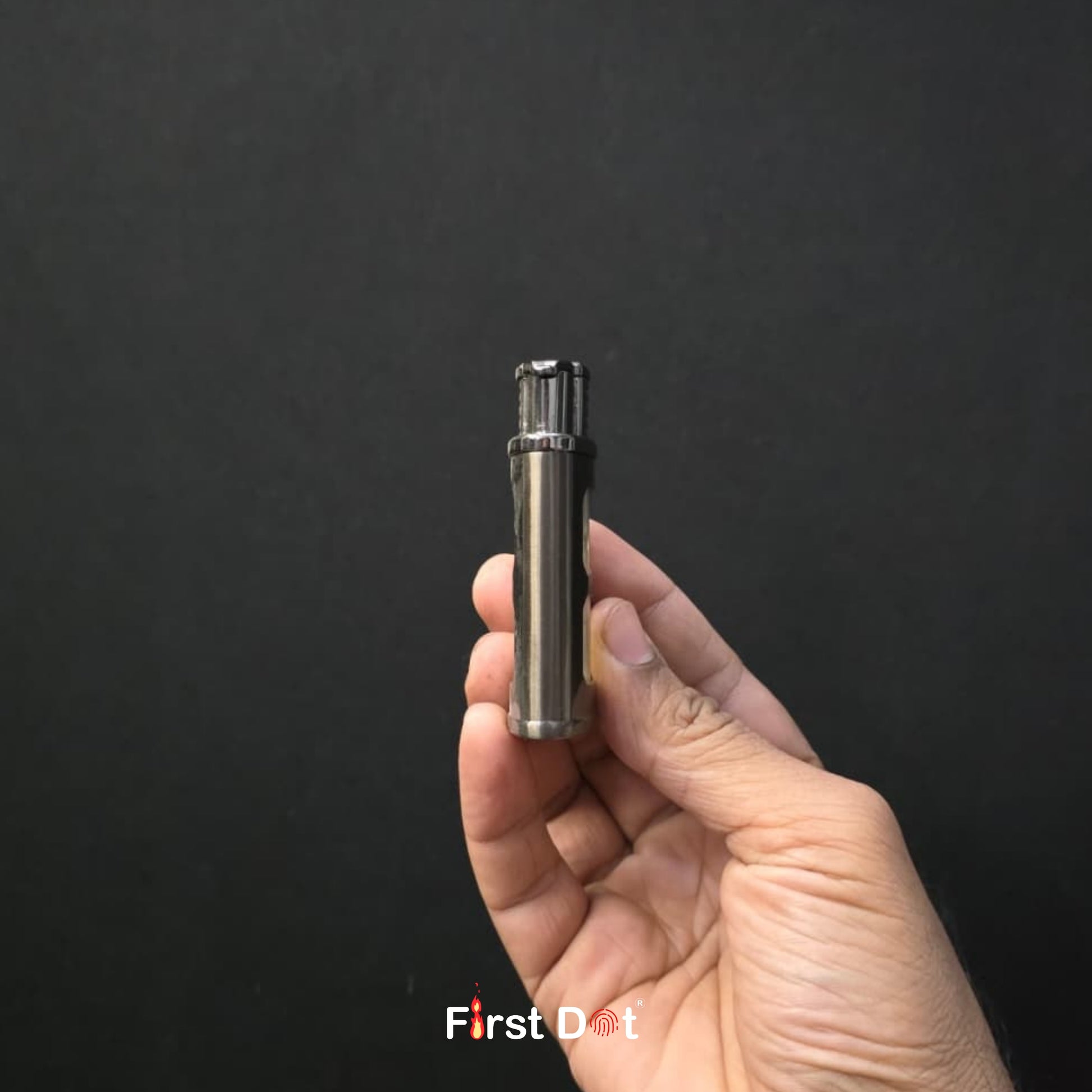 Hand holding a small metallic device against a black background with 'First Dot' branding.