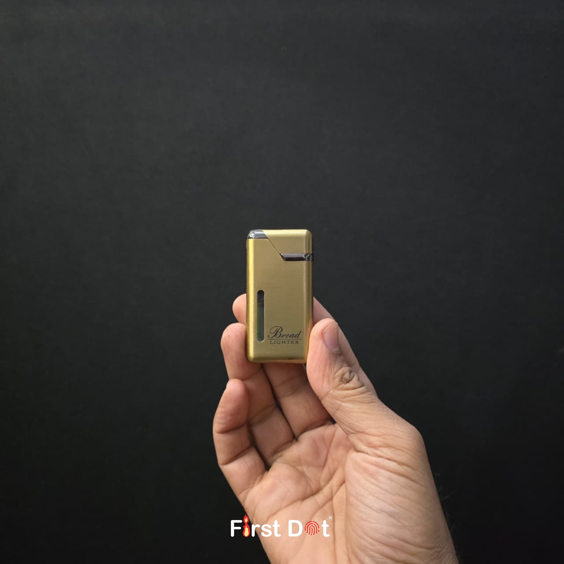 Hand holding a gold lighter against a black background with 'First Dot' branding.