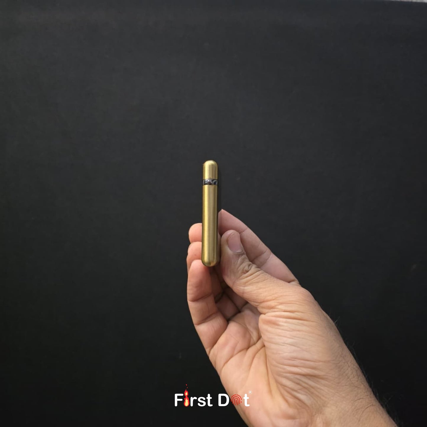 Hand holding a gold cylindrical object against a black background with 'First Dot' branding.