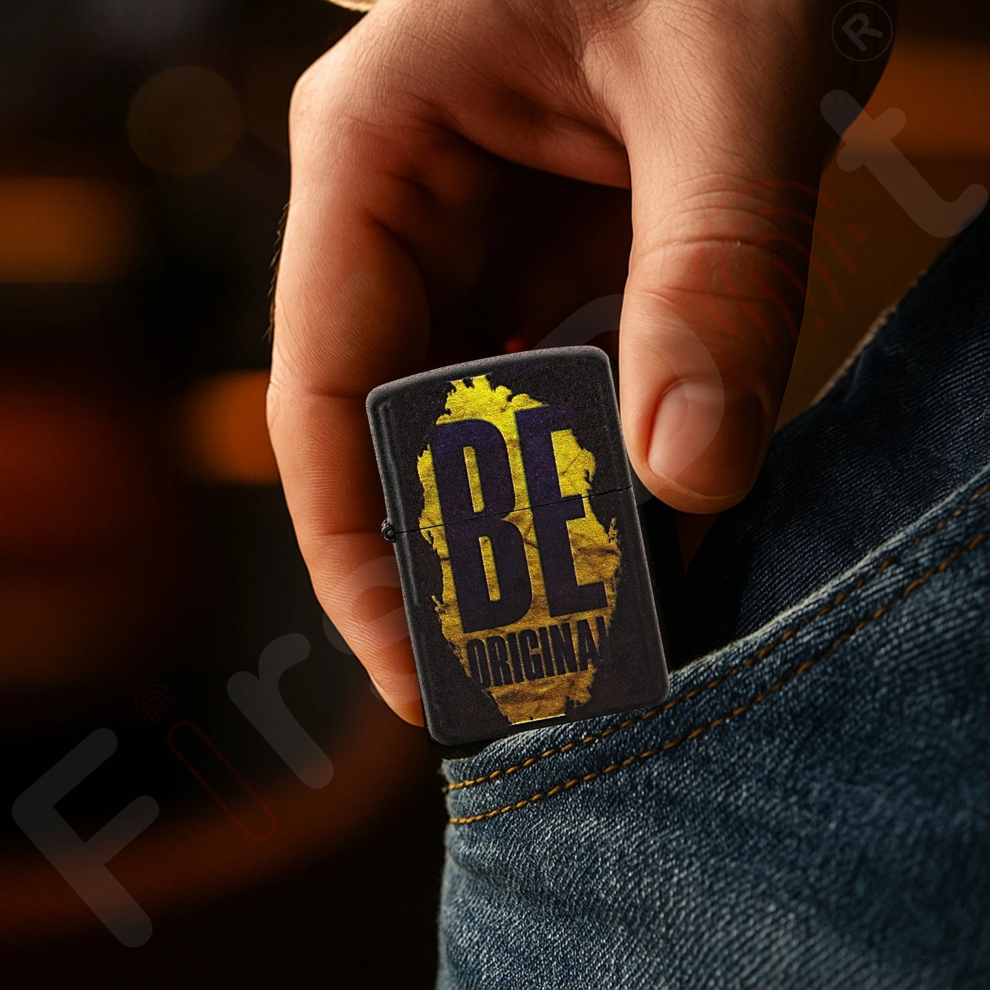 Hand holding a First Dot lighter with 'BE ORIGINAL' design against a blurred Be Original Premium Refillable Cigarette Lighter – powered by liquid fuel, strong flame, sleek design, and made to stand out with every spark.background