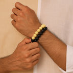 Hand wearing a black and yellow beaded bracelet against a beige  CrackleStoneBraceletbackground