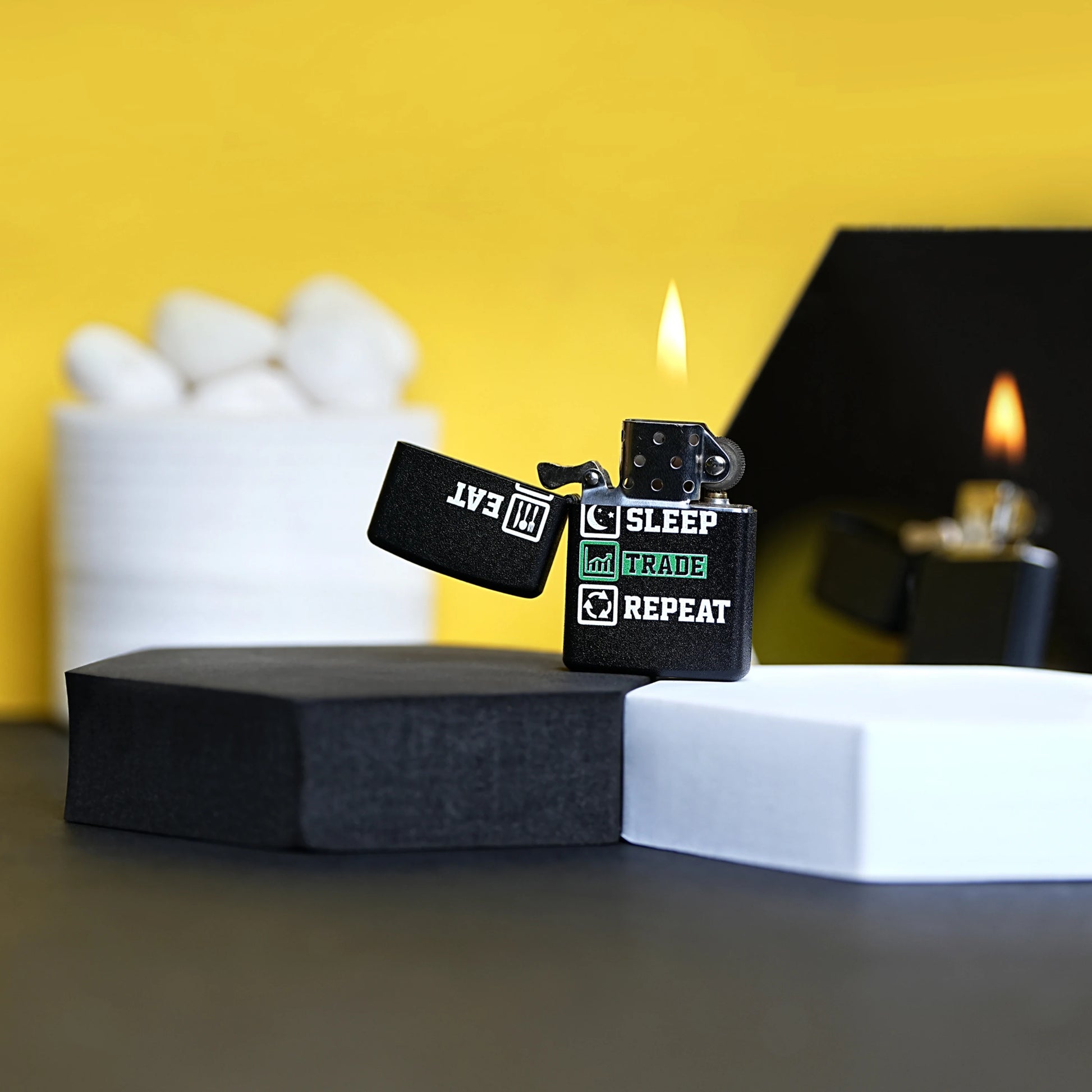 Two black lighters with text on a black stand against a yellow background Eat Sleep Trade Repeat Refillable Cigarette Lighter