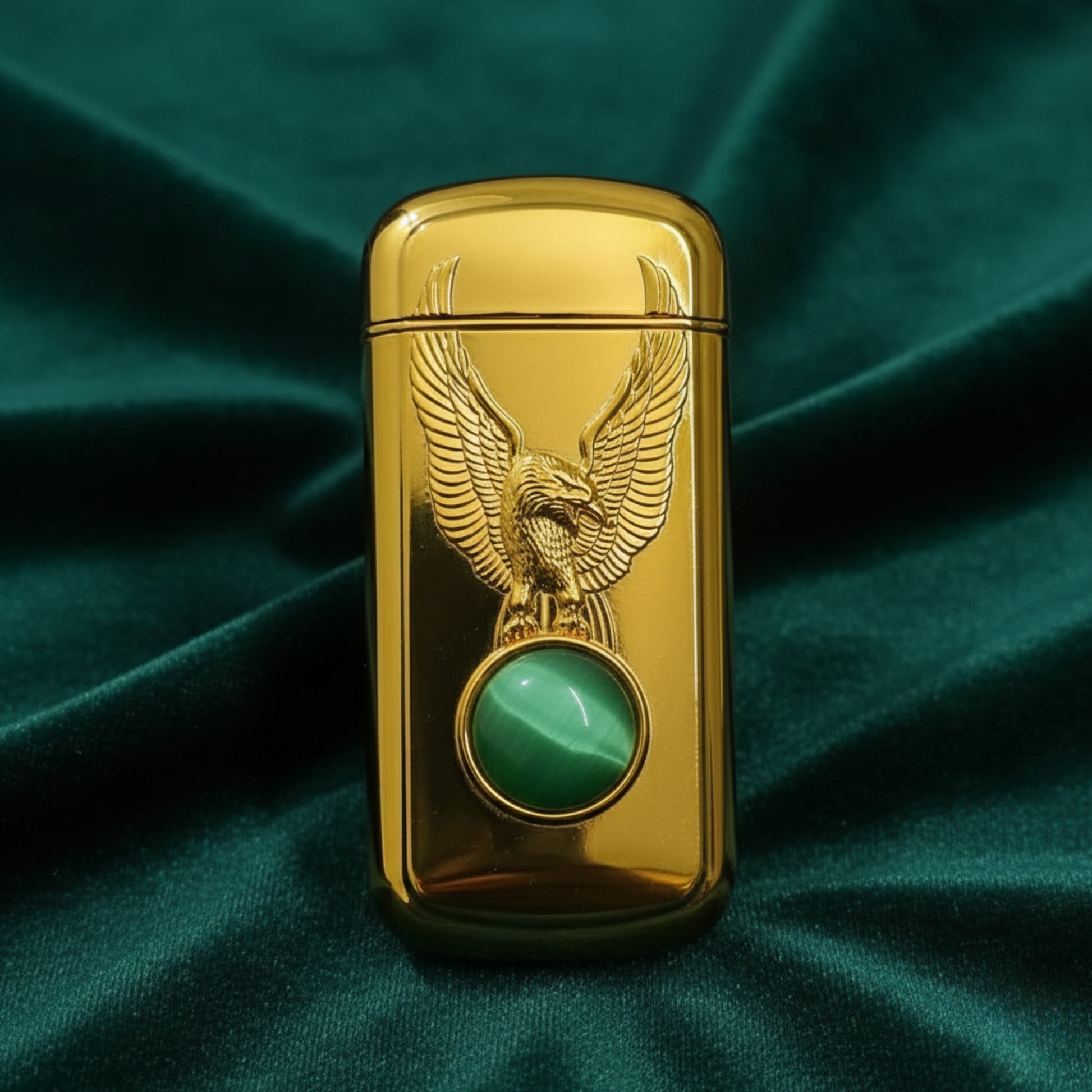 Gold lighter with eagle design and green gemstone on a green fabric background