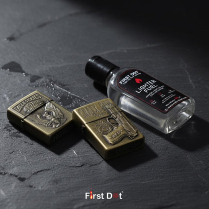 Two brass lighters and a bottle of lighter fuel on a dark surface with 'First Dot' branding.
