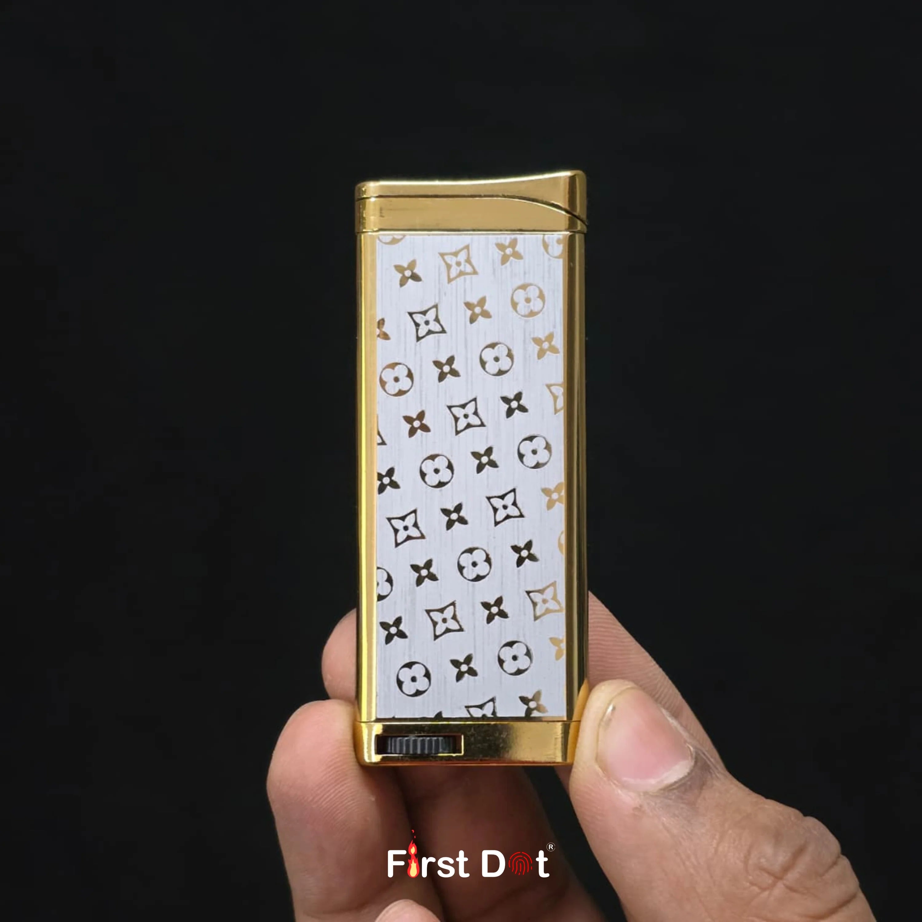 Gold lighter with patterned design held by a hand against a black background