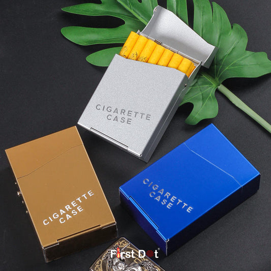 Three cigarette cases in gold, silver, and blue on a dark surface with green leaves.