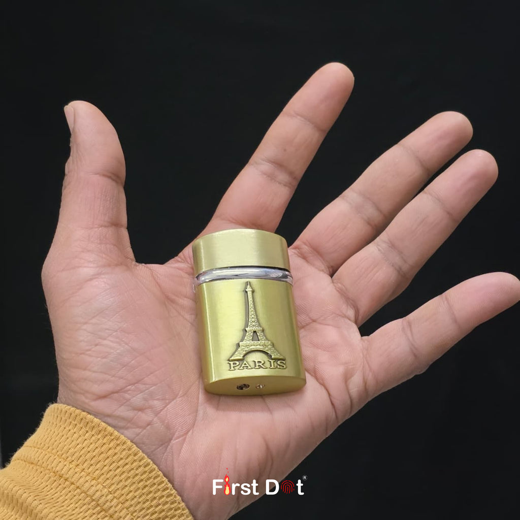 Gold cylindrical lighter with Eiffel Tower design held in a hand against a black background, featuring 'First Dot' branding.