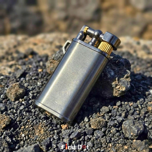 Metallic lighter on a rocky surface with 'First Dot' branding.