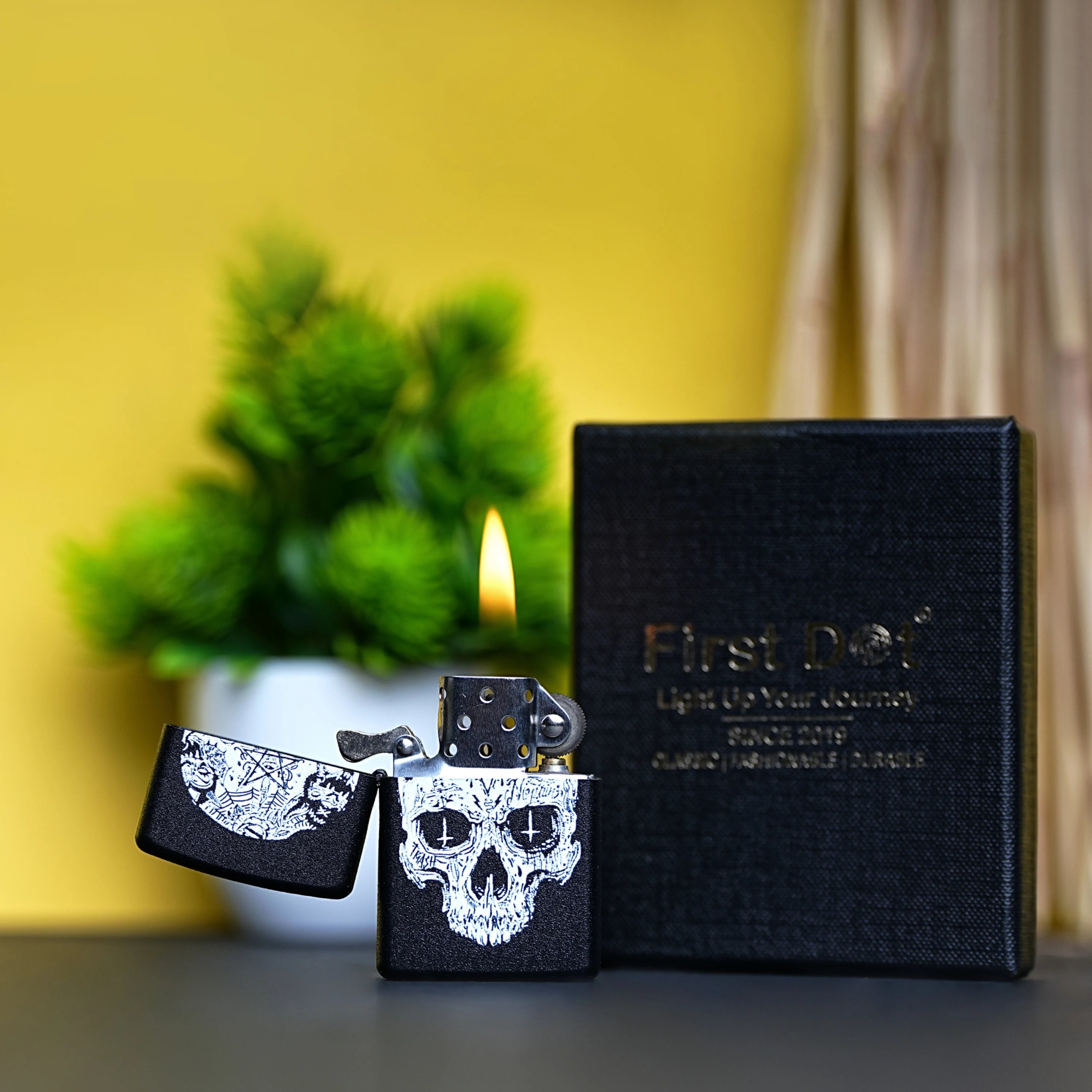 Black lighter with skull design, open, next to a black case labeled 'First Dot' on a blurred background. Inverted Cross Skull Premium Refillable Cigarette Lighter