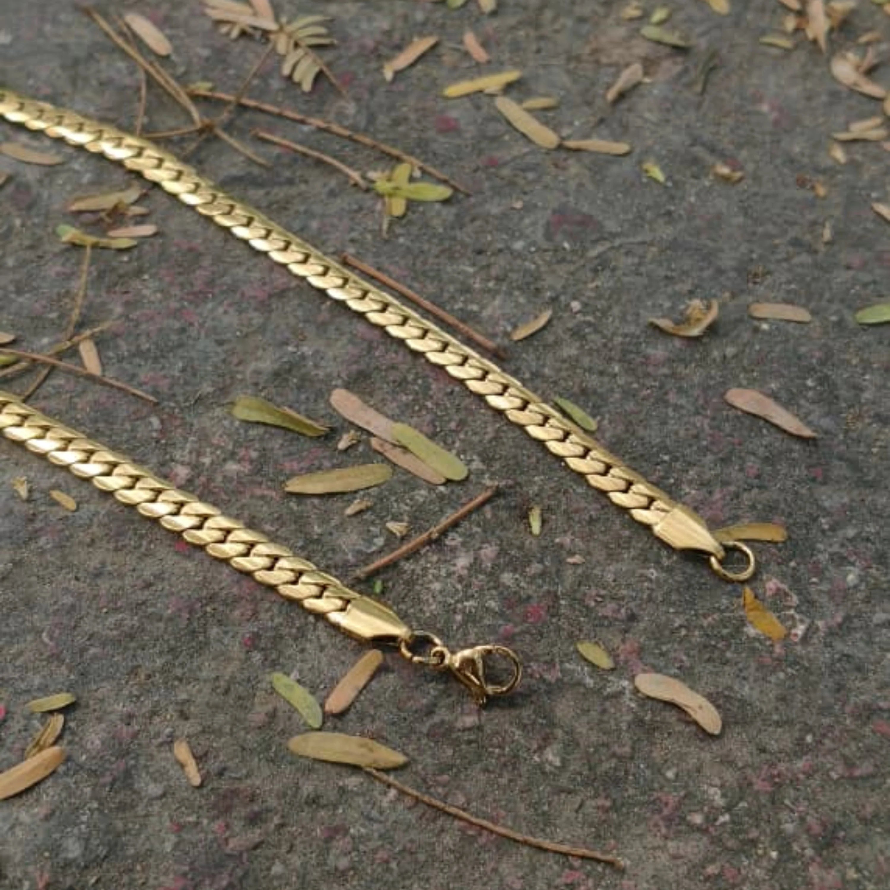 Gold chain on a textured surface with leaves First Dot Italian Golden Curb Chain for Men