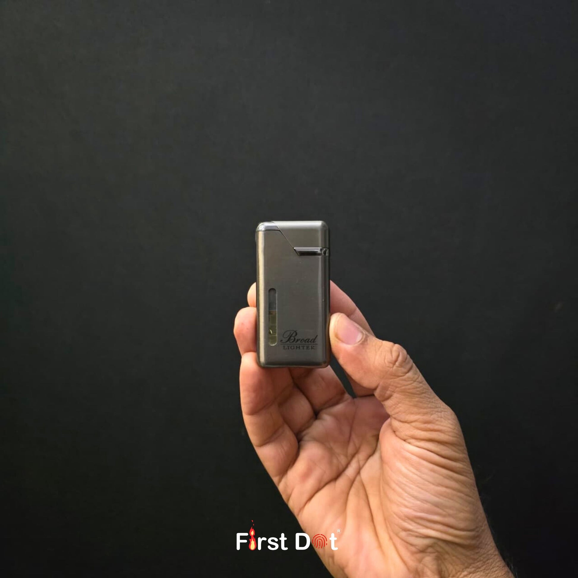 Hand holding a small metallic object against a black background