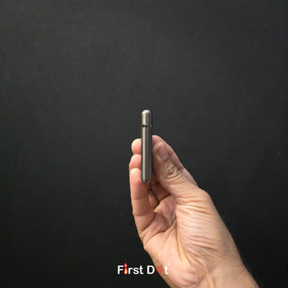 Hand holding a small metallic device against a black background with 'First Dot' branding.