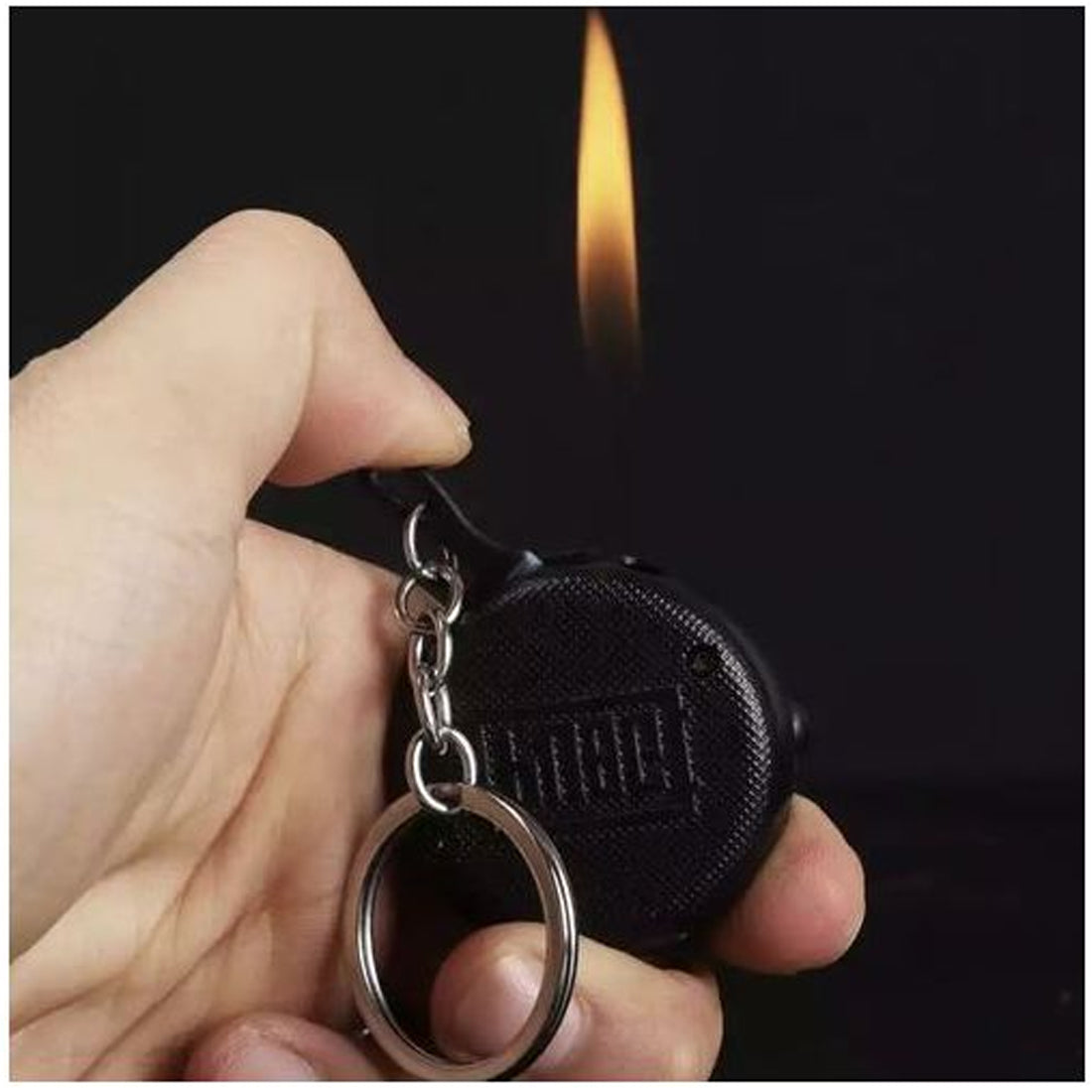 Hand holding a black keychain lighter with flame in the background