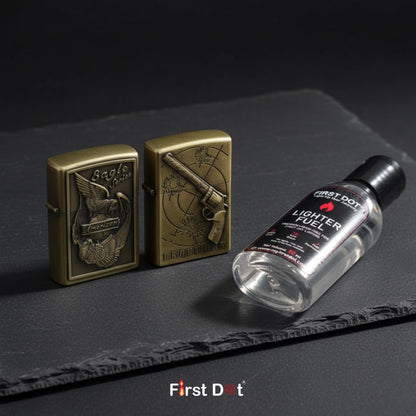 Two brass lighters and a bottle of lighter fuel on a dark surface with 'First Dot' branding.