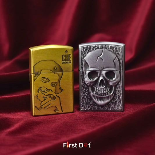 Two lighters, one gold with a face engraving and the other silver with a skull design, on a red fabric background. First Dot brand visible.