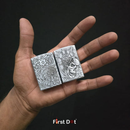 Two silver zippo lighters with intricate designs held in a hand against a black background, featuring the 'First Dot' brand.