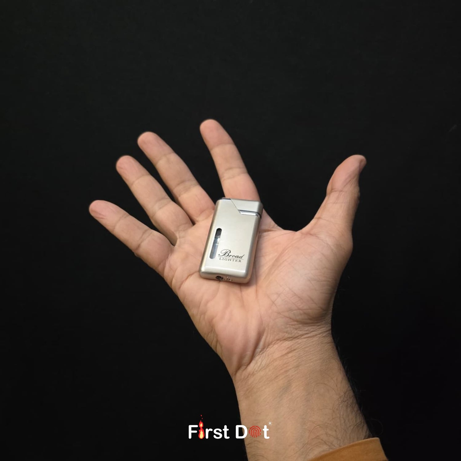Hand holding a small silver lighter with 'Briquet' branding against a black background