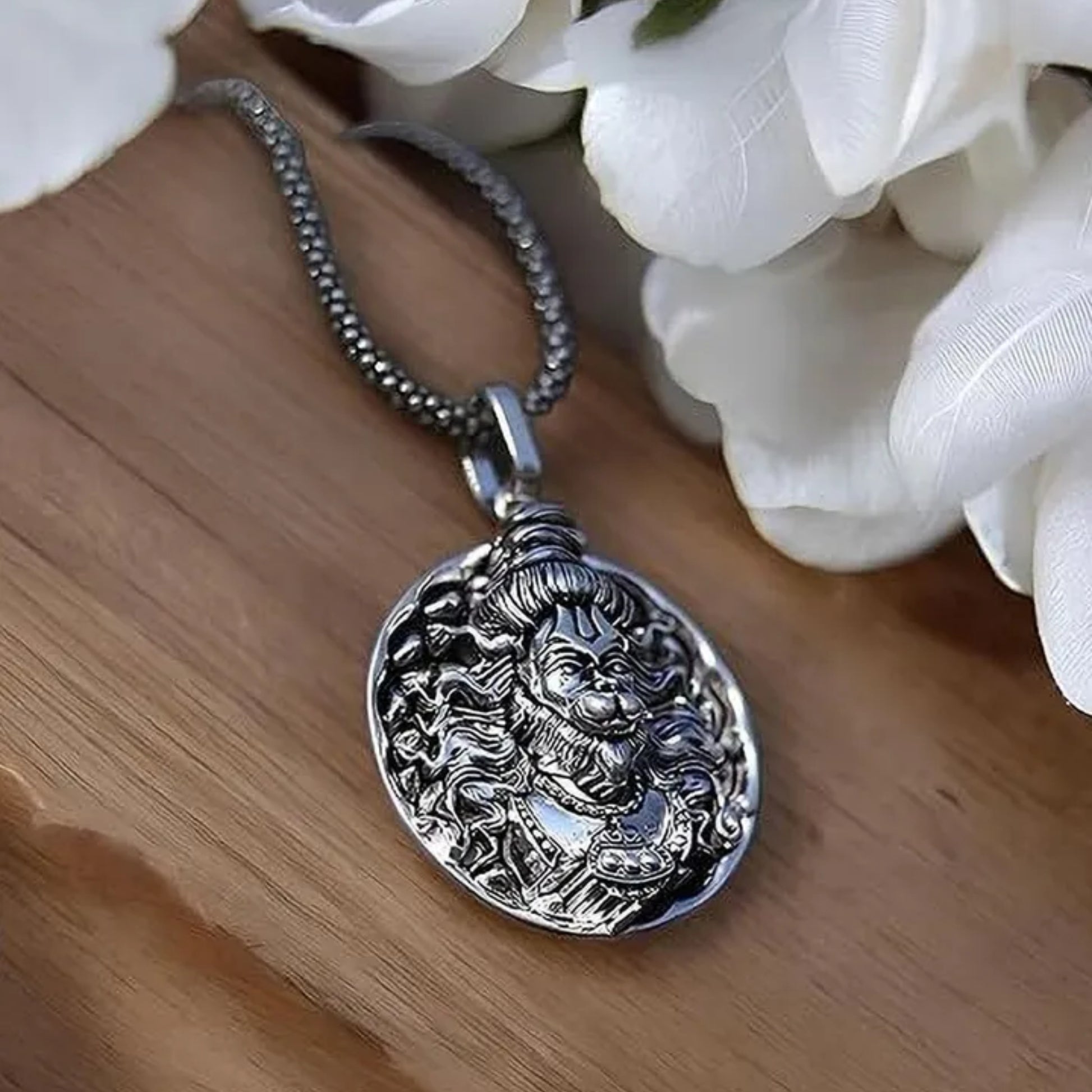Silver pendant necklace on a wooden surface with white flowers in the background श्री हनुमान जी Round Pendant Locket with Chain 