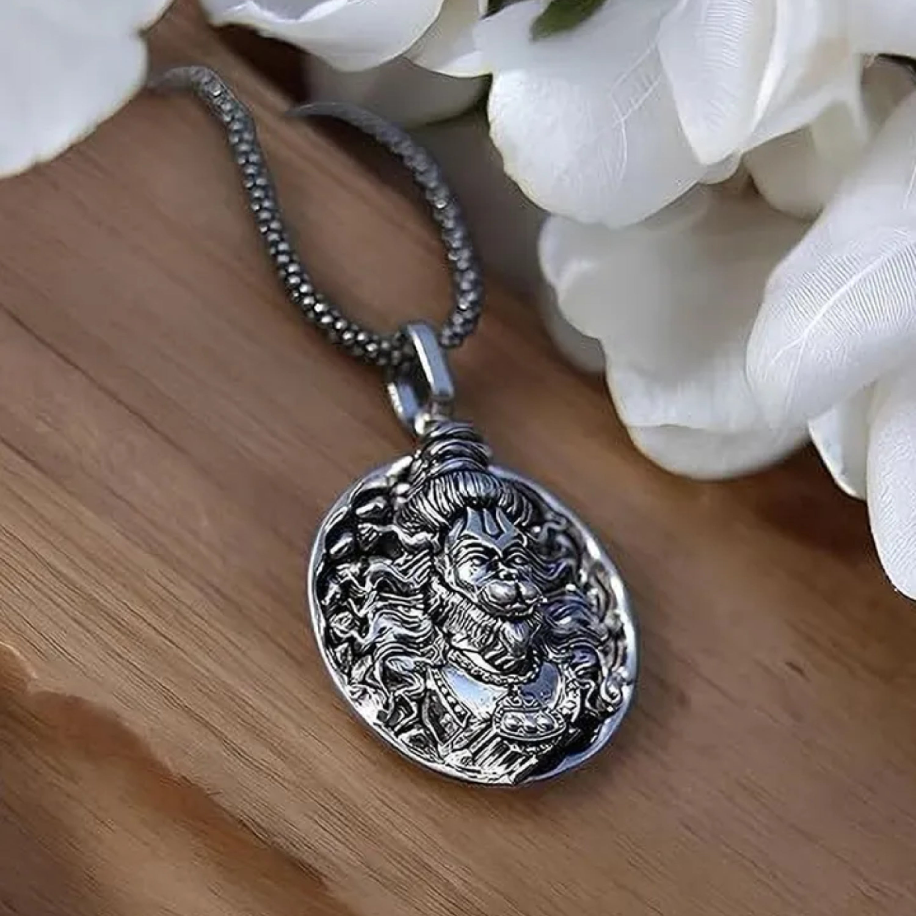 Silver pendant necklace on a wooden surface with white flowers in the background श्री हनुमान जी Round Pendant Locket with Chain 