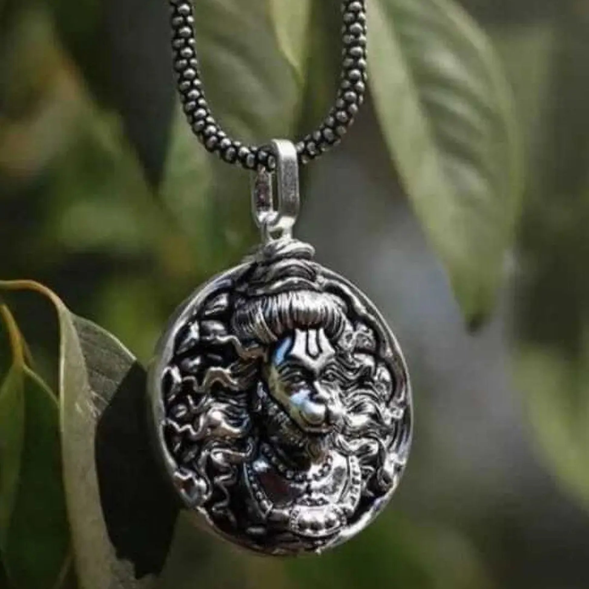 Silver pendant necklace with intricate design on a blurred green leaf background श्री हनुमान जी Round Pendant Locket with Chain 