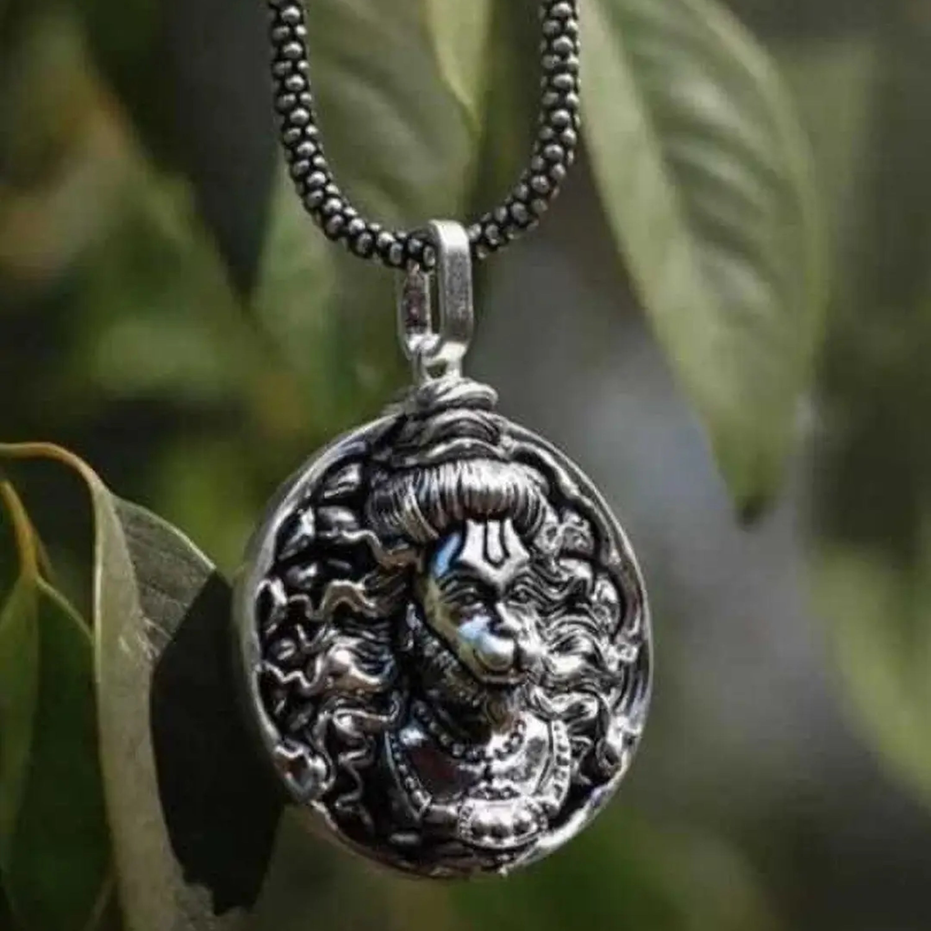 Silver pendant necklace with intricate design on a blurred green leaf background श्री हनुमान जी Round Pendant Locket with Chain 