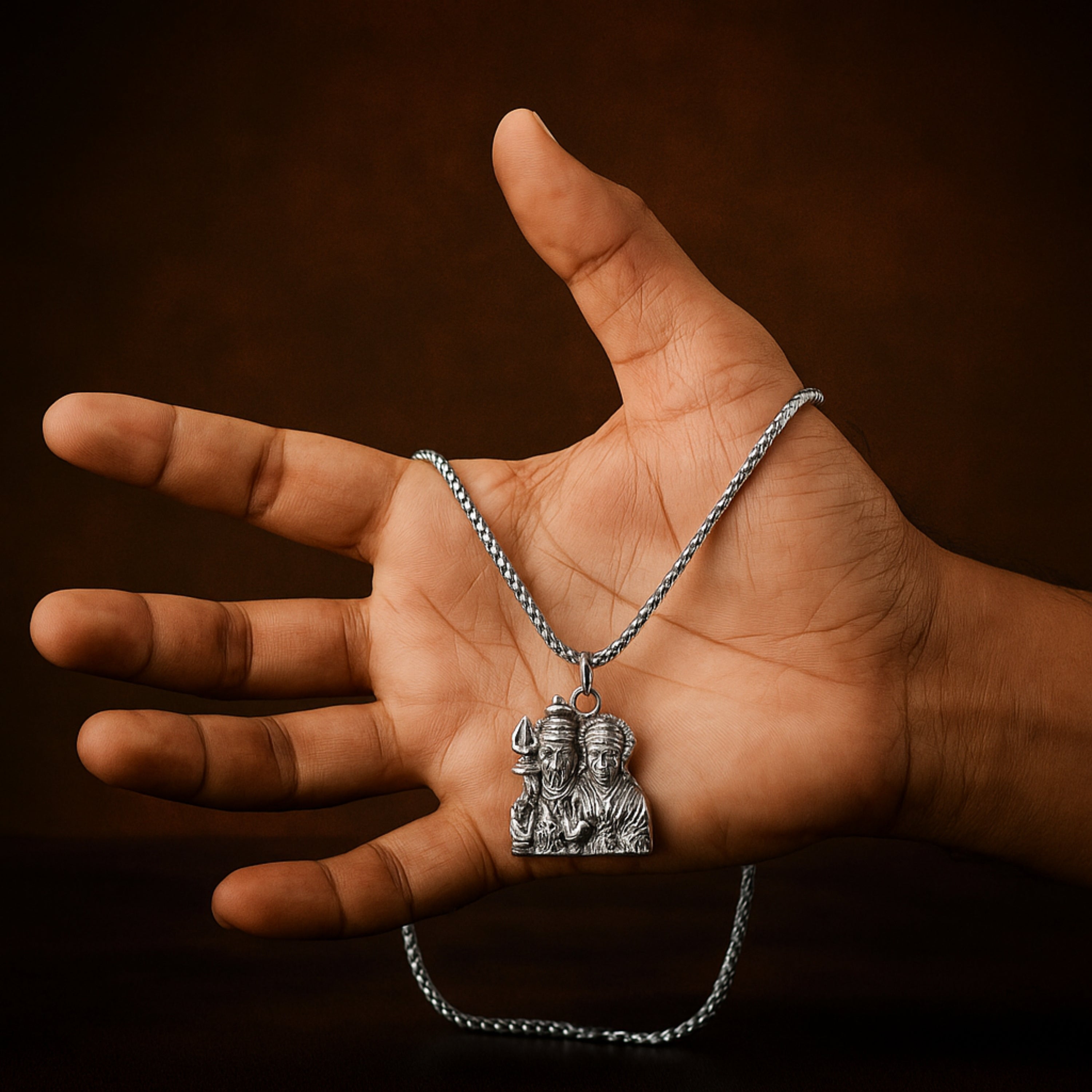 Hand holding a silver necklace with a pendant featuring two figures against a dark background ShivaParvati LocketwithChain