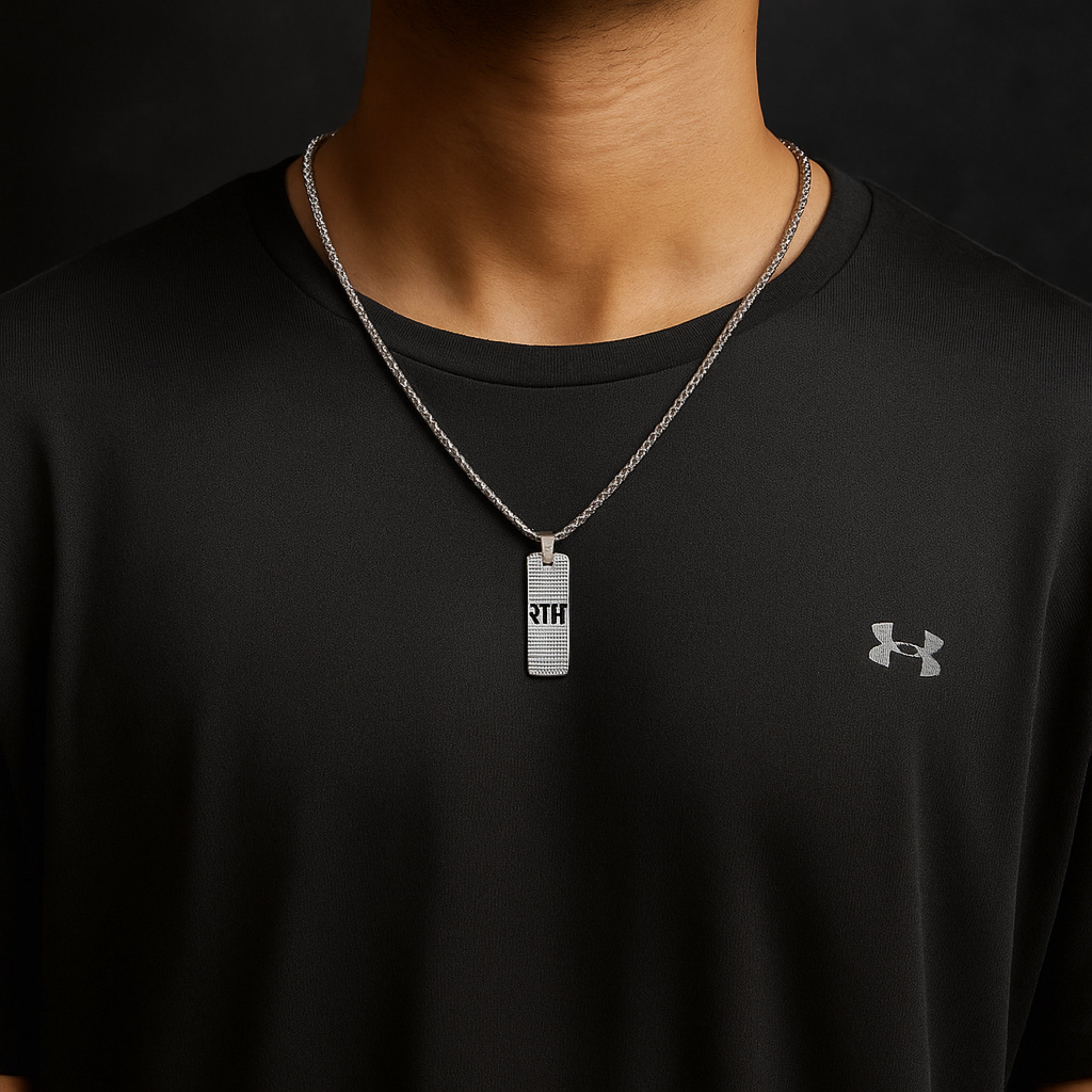 Person wearing a black Under Armour shirt with a necklace featuring a rectangular pendant. Silver necklace with a pendant on a wooden surface ShriRam NaamPendantLocketwithChain
