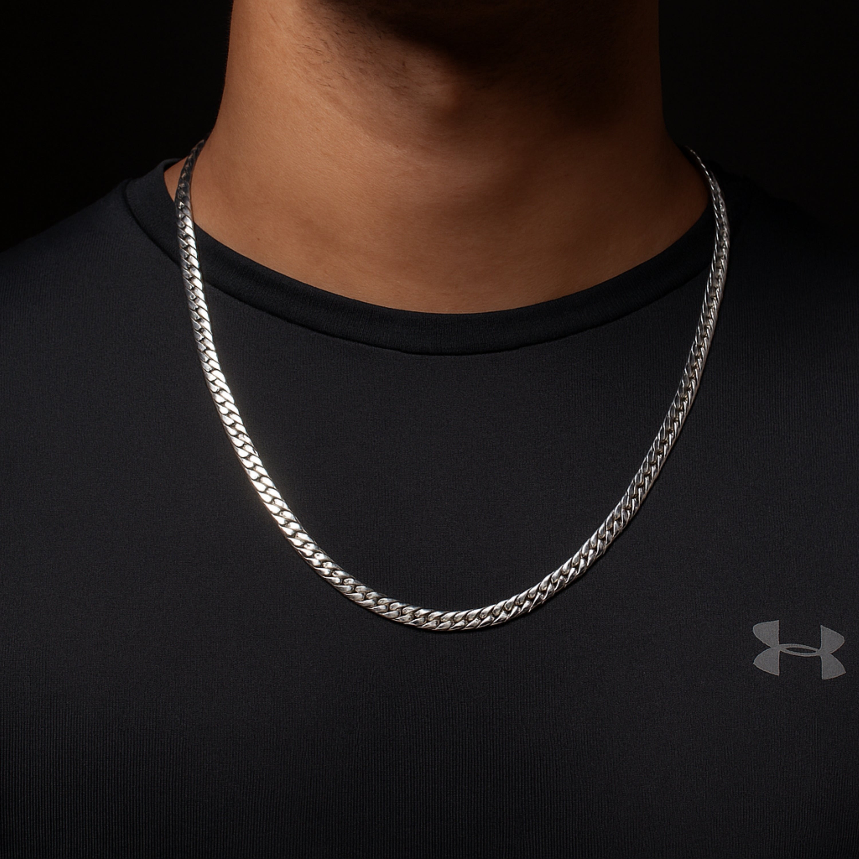 Silver chain necklace on a person wearing a black Under Armour shirt.