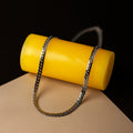 Silver chain draped over a yellow cylindrical object on a brown surface with black background