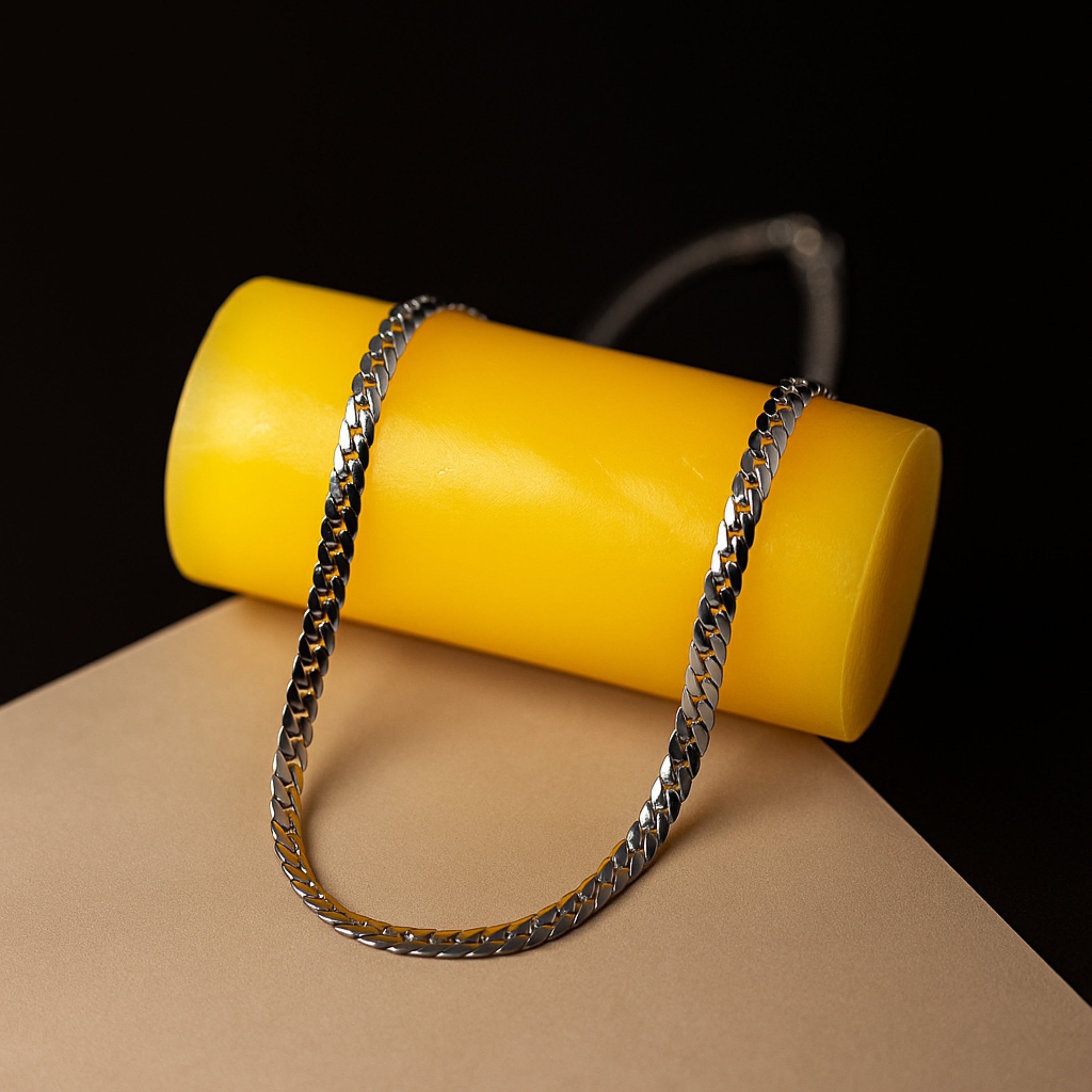 Silver chain draped over a yellow cylindrical object on a brown surface with black background