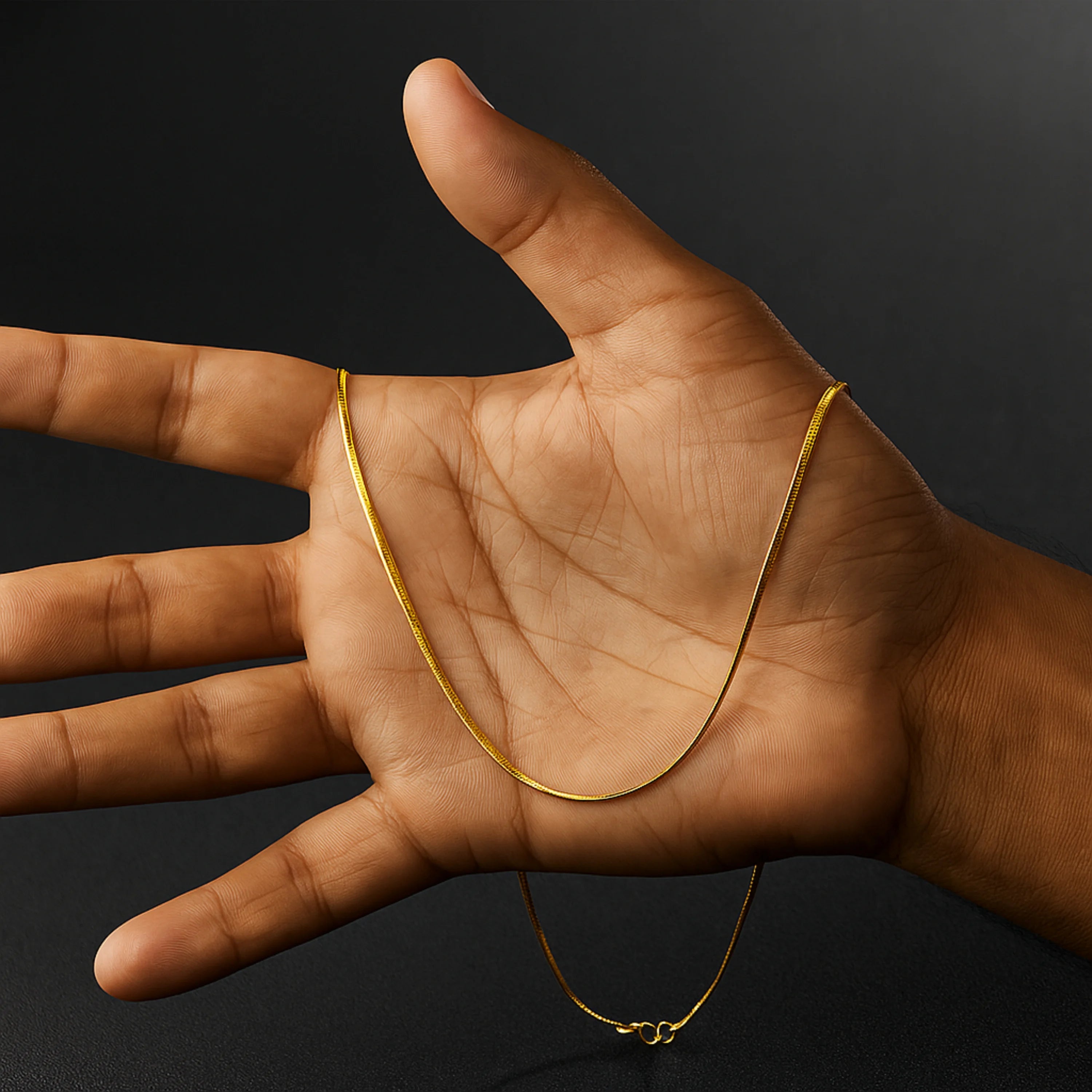 Gold chain necklace held in a hand against a black background nakeChainNecklace