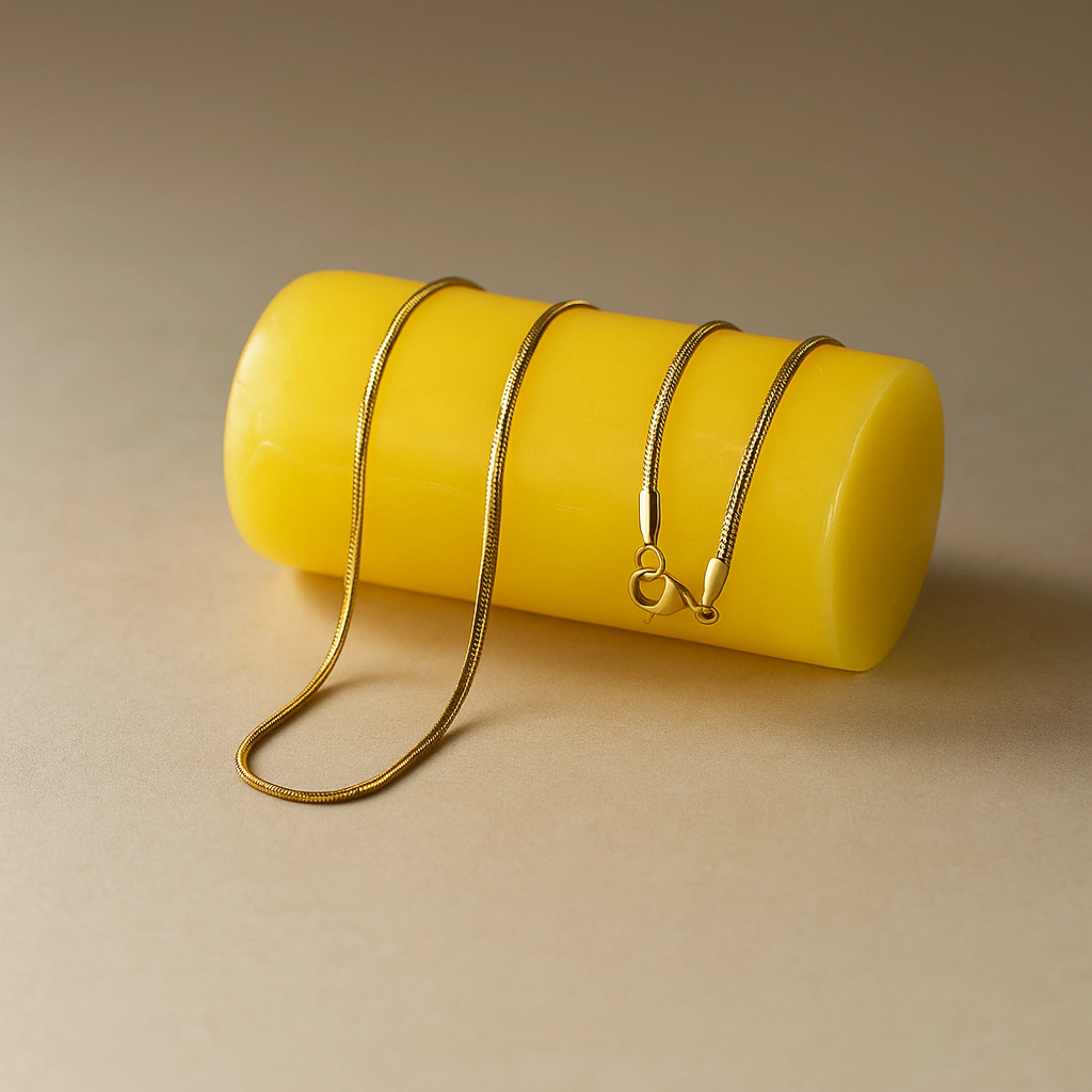 Gold necklace on a yellow cylindrical object against a beige background nakeChainNecklace