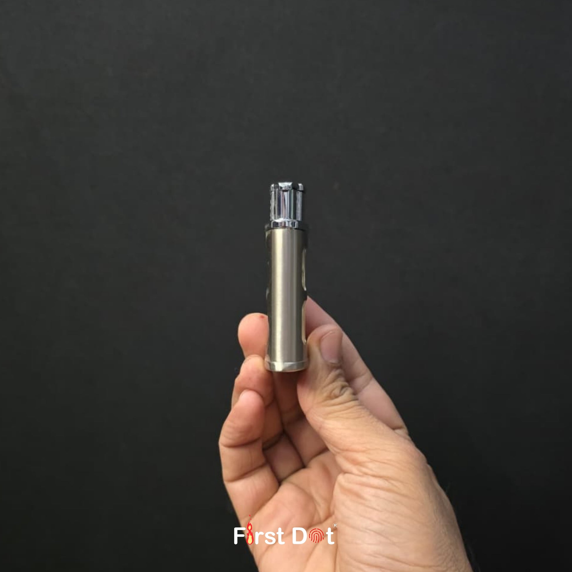 Hand holding a small metallic device against a black background with 'First Dot' branding.