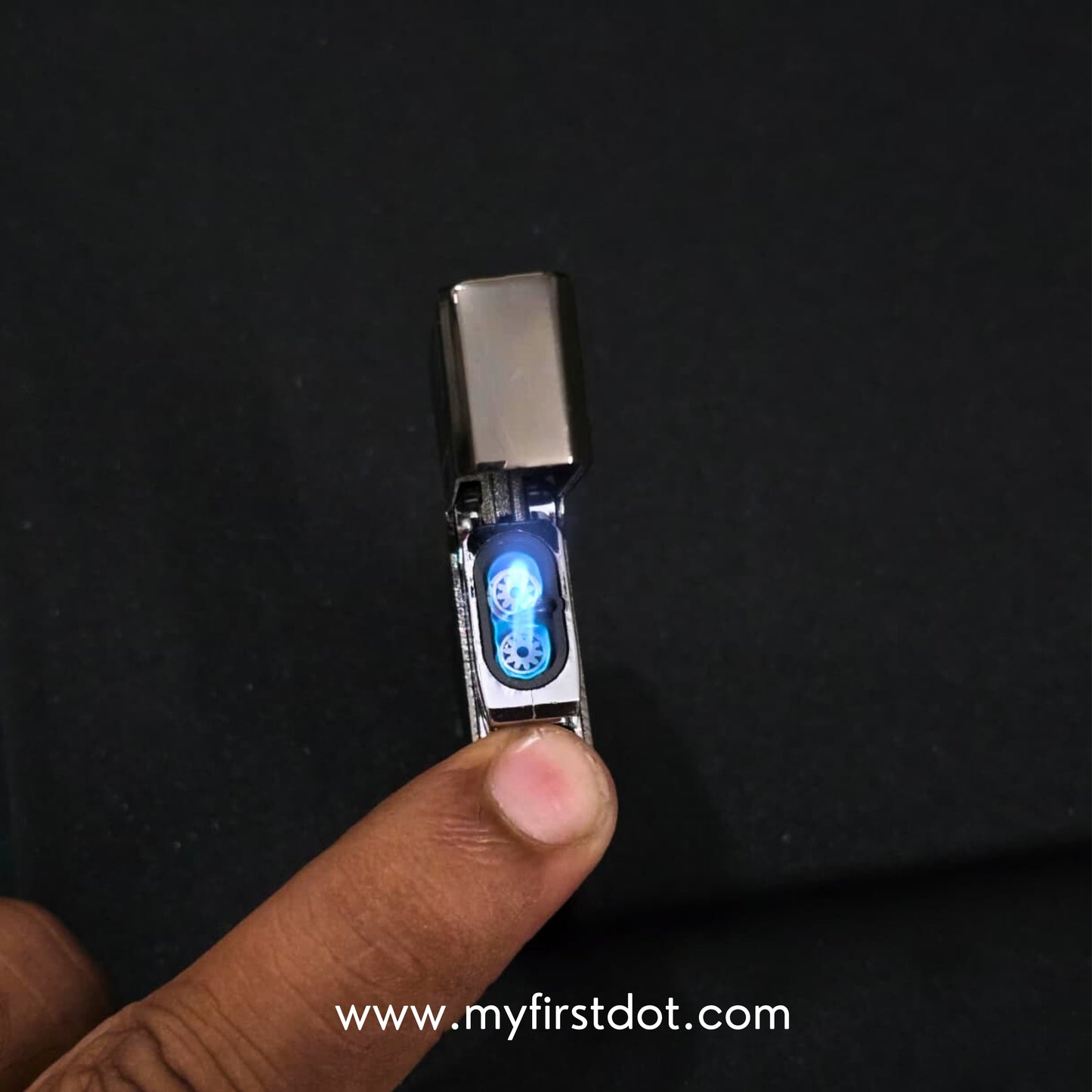 Small electronic device with a blue light on a dark background, held by a finger. Monarch Double Flame Torch Lighter Brushed Grey