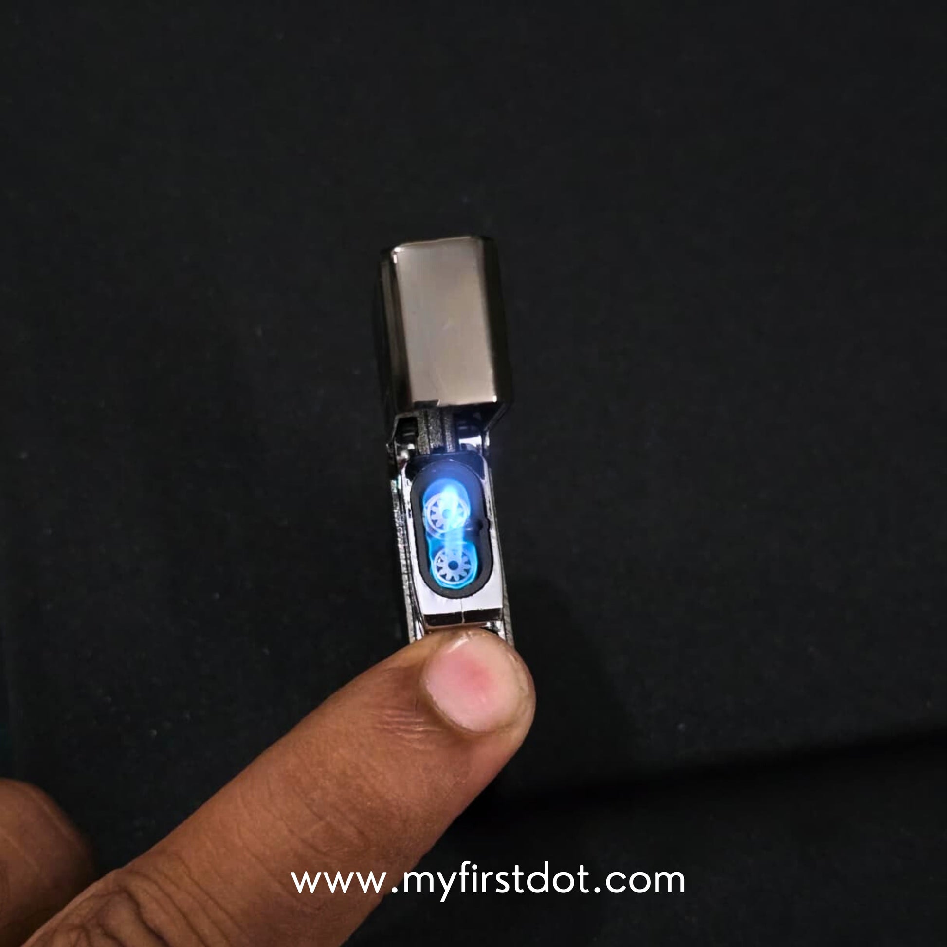 Small electronic device with a blue light on a dark background, held by a finger. Monarch Double Flame Torch Lighter Brushed Grey